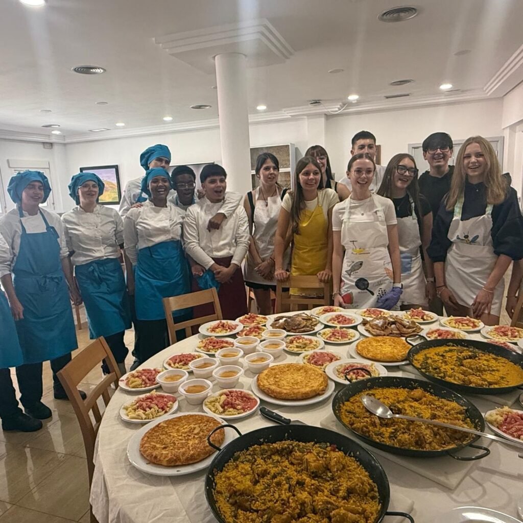 Foto de grupo del alumnado y el profesorado con la mesa llena de platos elaborados: paellas, tortillas y natillas