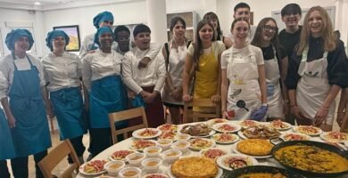 Foto de grupo del alumnado y el profesorado con la mesa llena de platos elaborados: paellas, tortillas y natillas