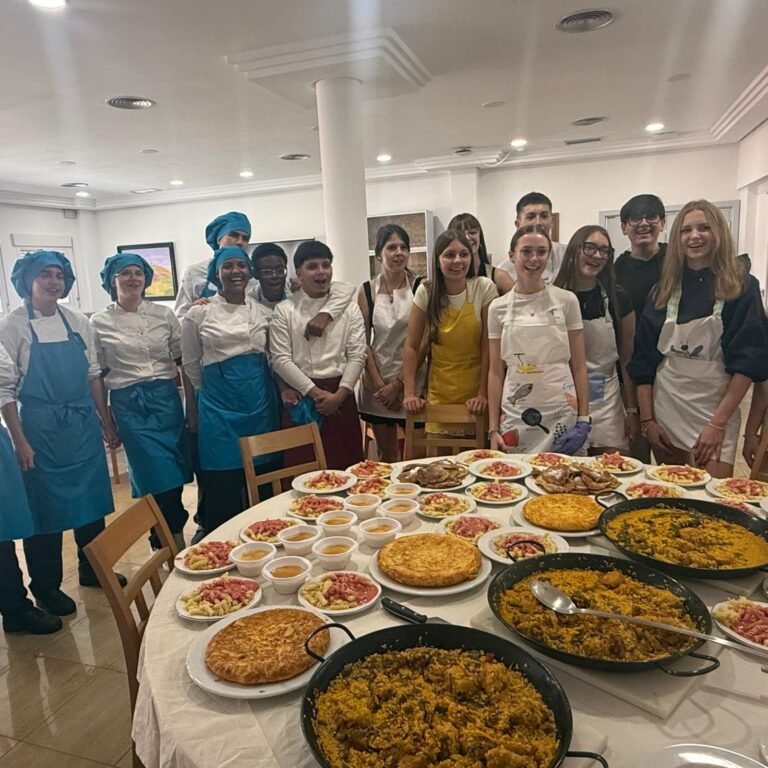 Foto de grupo del alumnado y el profesorado con la mesa llena de platos elaborados: paellas, tortillas y natillas